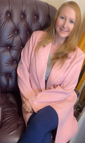 A woman in a pink blazer sitting on a dark leather chair.
