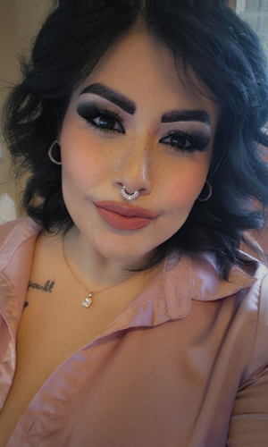 Close-up of a smiling woman with makeup and a septum piercing.